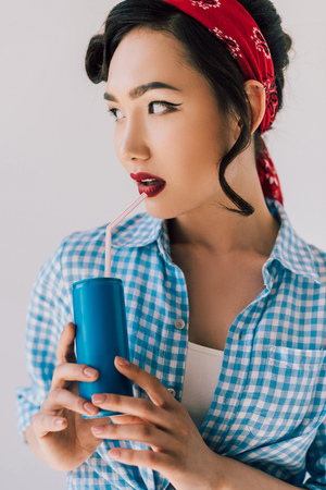 portrait of beautiful asian woman with soda drink in hands looking away isolated on greyの写真素材