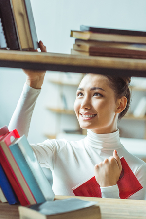 beautiful smiling asian student choosing books in libraryの写真素材
