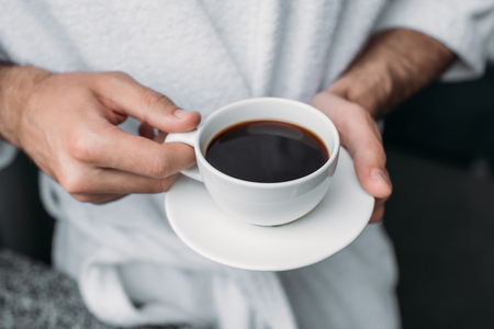 cropped shot of man in bathrobe holding cup of coffee at morningの写真素材