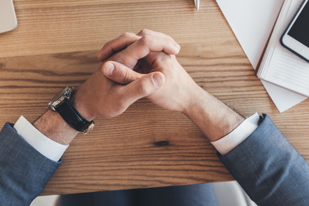 Cropped shot of male hands clasped together on wooden deskの写真素材