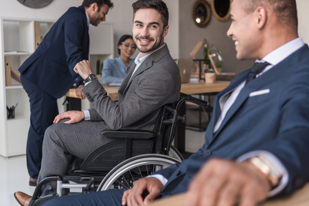 selective focus of smiling disabled businessman and colleagues in officeの写真素材
