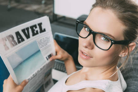 gorgeous blonde woman reading travel newspaper on sofa in living roomの写真素材