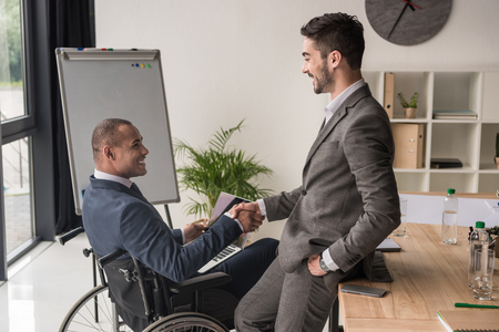 side view of smiling multiethnic businessmen shaking hands at workplaceの写真素材