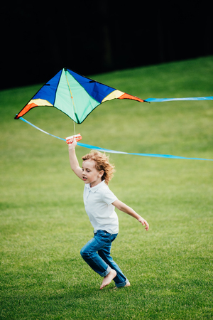 adorable little boy playing with kite and running on green grass at parkの写真素材