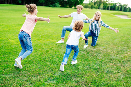 happy parents with open arms looking at cute little children running on grassの写真素材