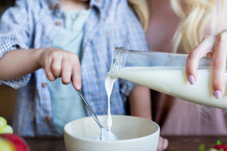 cropped shot of mother and son pouring milk in bowl for breakfast  の写真素材