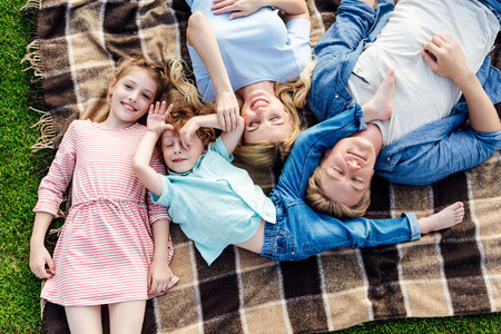 top view of happy young family with two children lying on plaid at picnic