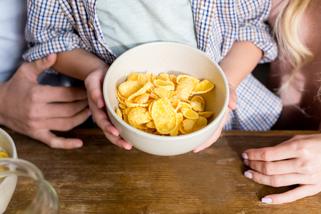 cropped shot of parents and child holding bowl with corn flakes for breakfastの写真素材