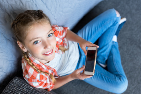 overhead view of cute little girl using smartphone and smiling at cameraの写真素材