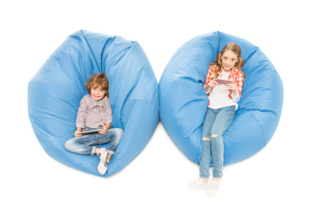 overhead view of kids with digital devices resting on bean bag chairs isolated on whiteの写真素材