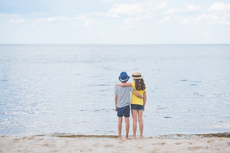 back view of girl and boy hugging each other while standing at seasideの写真素材