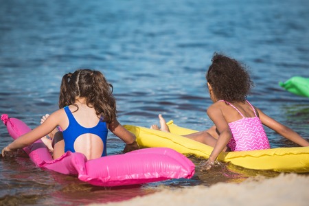 back view of little girls in swimsuits on inflatable mattresses at sea の写真素材