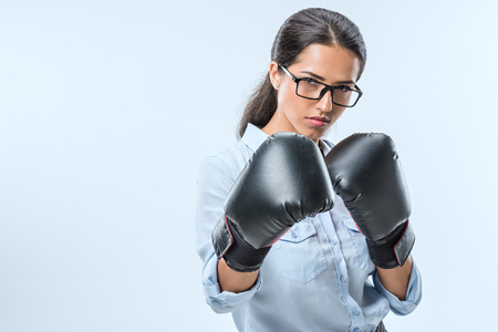 portrait of serious businesswoman in boxer gloves looking  at camera isolated on blueの写真素材