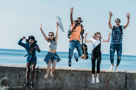 multicultural group of young friends jumping of parapet together