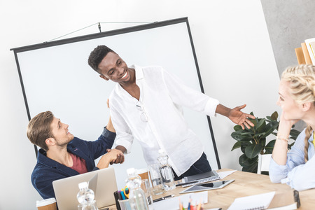 multiethnic happy business partners shaking hands at meeting in conference room
