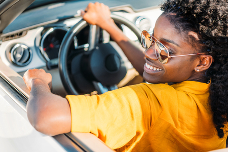 portrait of smiling african american woman in sunglasses riding carの写真素材