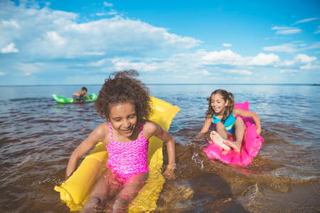 multicultural happy girls swimming on inflatable mattresses at sea togetherの写真素材