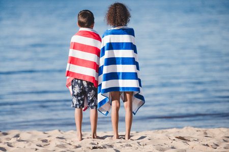 back view of boy and girl in towels standing together on seashoreの写真素材
