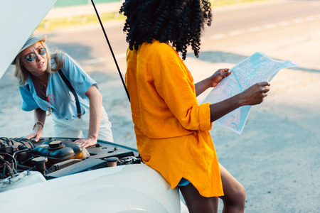 african american woman looking for destination on map while friend checking broken carの写真素材