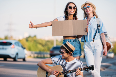 multicultural friends with empty cardboard hitchhiking while traveling togetherの写真素材