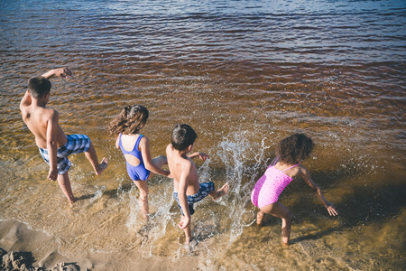 back view of group of little kids in swimsuits playing at beachの写真素材