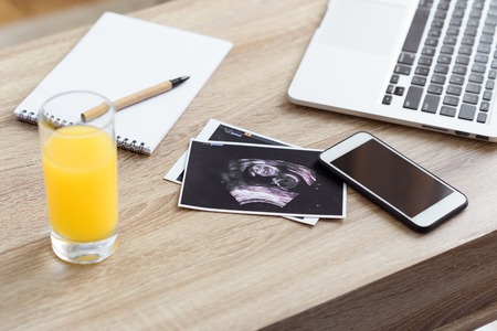 glass of juice, ultrasound scan of unborn baby and digital devices on wooden tabletopの写真素材