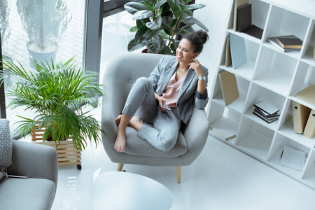 high angle view of smiling african american businesswoman with smartphone resting on armchairの写真素材