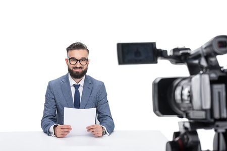 smiling male newscaster with papers sitting in front of camera, isolated on white の写真素材