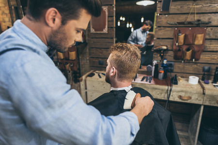 Handsome bearded man is getting hairstyle by hairdresser at barber shopの写真素材