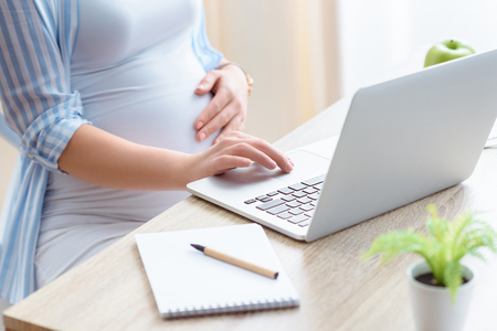 cropped view of pregnant woman using laptop and notepad at homeの写真素材