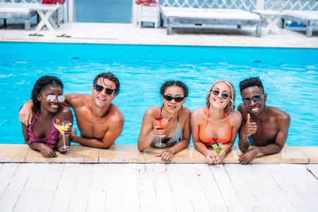 Group of young happy multiethnic people with cocktails in swimming pool の写真素材