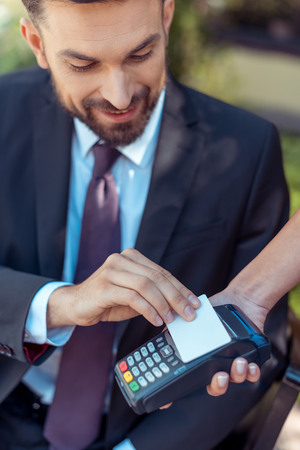Close-up view man using contactless credit card on pos terminalの写真素材