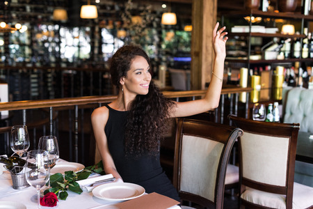 Portrait of young beautiful woman with raised hand calling waiter in restaurantの写真素材