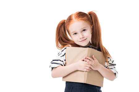 adorable redhead schoolgirl hugging book and smiling at camera isolated on whiteの写真素材