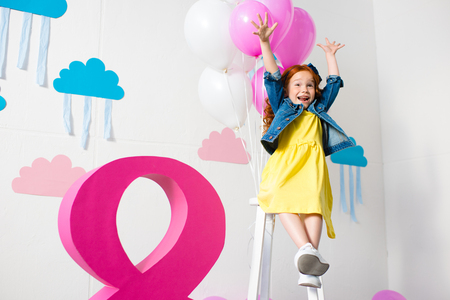 happy little redhead girl raising hands while having fun at birthday partyの写真素材