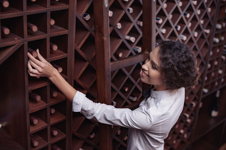 Portrait of young beautiful woman sommelier choosing wine in cellar
