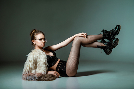 attractive fashionable young woman posing in black sexy clothes and fur coat on greyの写真素材