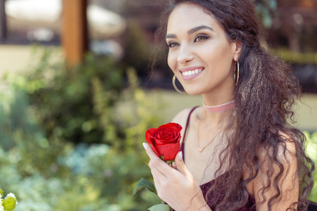 Close-up portrait of beautiful young woman sitting with red rose and smiling の写真素材