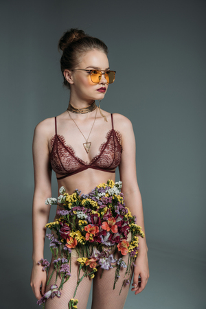 young sensual beautiful girl posing in floral skirt, lace bra and orange sunglasses for fashion shoot, isolated on greyの写真素材