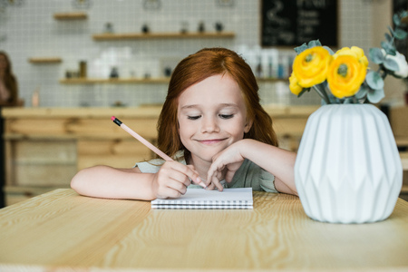 adorable smiling redhead girl drawing with pencil in cafe