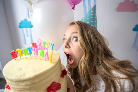 cute little girl in party cap biting birthday cake and looking at camera