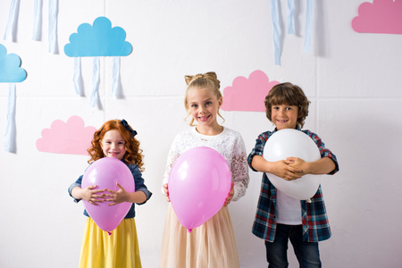 adorable happy kids holding balloons and smiling at camera at birthday party の写真素材