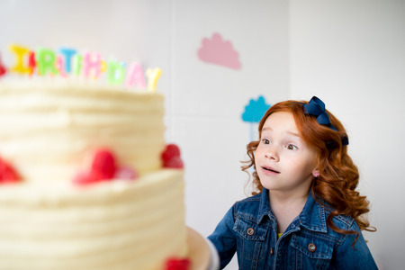 adorable surprised red haired girl looking at birthday cake 