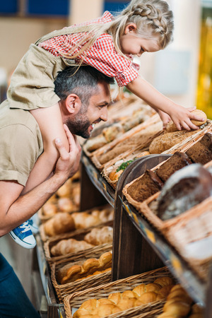 side view of happy father and daughter buying bread in supermarketの写真素材