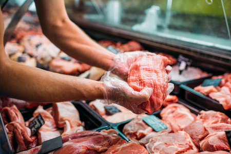 partial view of shop assistant holding fresh raw meat in supermarketの写真素材