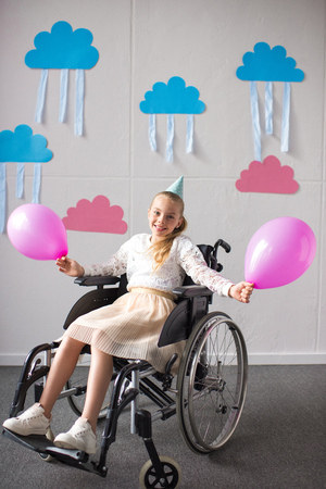 cheerful disabled girl holding balloons and smiling at camera at birthday partyの写真素材