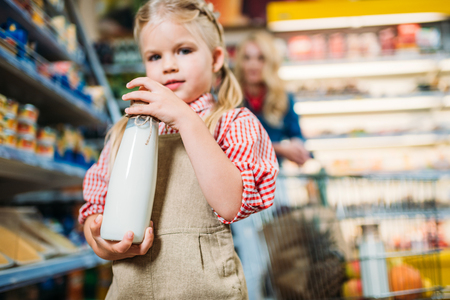 adorable little girl holding bottle of milk in supermarketの写真素材