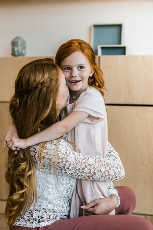 beautiful happy mother and cute redhead daughter hugging indoors の写真素材