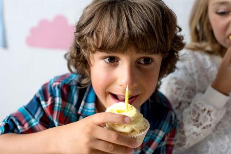 cute smiling boy eating cupcake with candle at birthday partyの写真素材