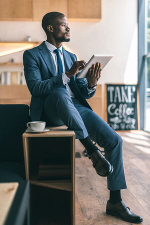 handsome thoughtful african american businessman using digital tablet during coffee break in cafe の写真素材